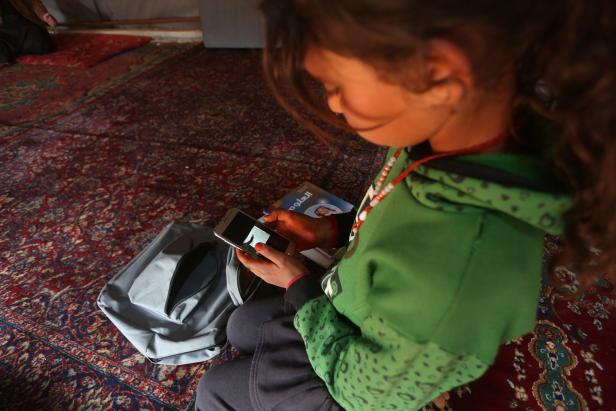 Die 9-jährige Maria verfolgt über das Handy ihres Vaters eine voraufgezeichnete Schulstunde in einem Zelt im Flüchtlingslager Idlib in Syrien