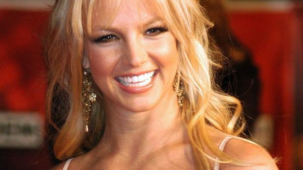 Britney Spears lächelt mit blonden Haaren und goldenen Ohrringen.