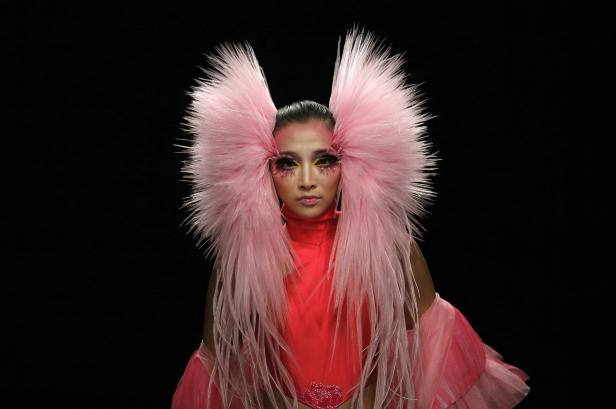 Eine Frau mit extravaganten, rosa Federn und auffälligem Make-up vor schwarzem Hintergrund.