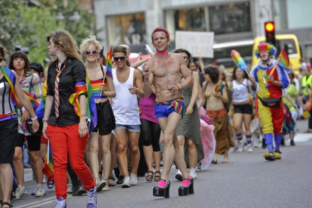 Eine Menschenmenge feiert auf einer Pride-Parade mit Regenbogenflaggen und farbenfrohen Kostümen.