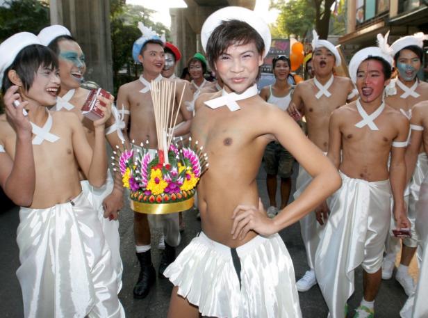 Eine Gruppe von Männern in weißen Kostümen nimmt an einer Parade mit Blumen und Räucherstäbchen teil.