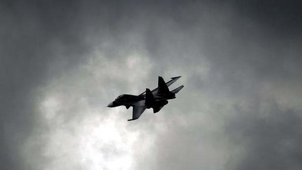 Ein Kampfjet fliegt vor einem dunklen, bewölkten Himmel.