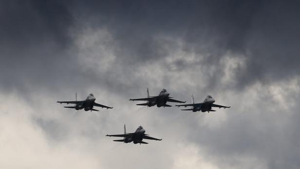 Vier Kampfflugzeuge fliegen in Formation vor einem bewölkten Himmel.