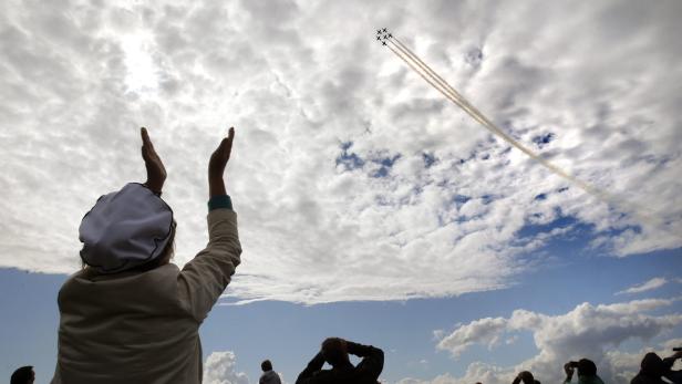 Zuschauer beobachten eine Flugstaffel am Himmel, die Rauchspuren hinterlässt.