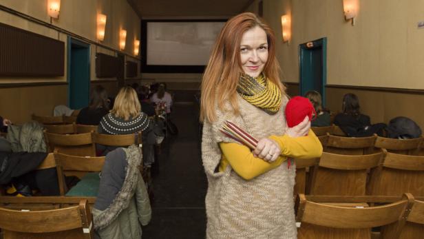 Eine Frau mit Stricknadeln und einem Wollknäuel steht in einem Kinosaal.