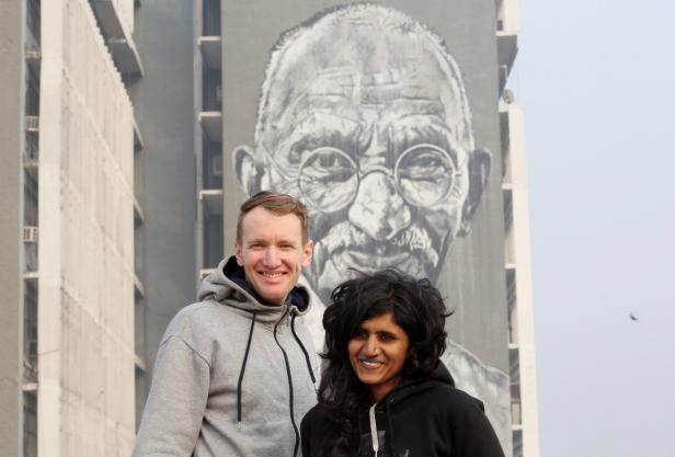 Zwei Personen stehen vor einem Gebäude mit einem großen Porträt von Mahatma Gandhi.
