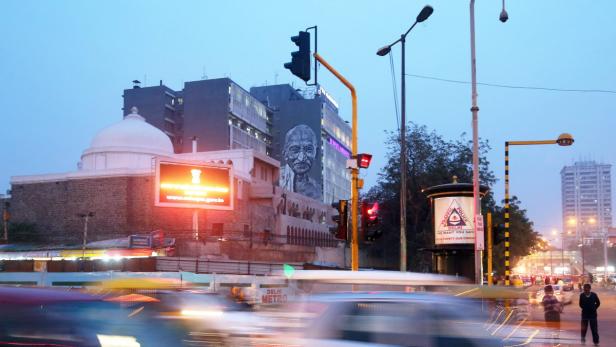 Ein belebter Verkehrsknotenpunkt in Delhi mit einem Porträt von Mahatma Gandhi an einem Gebäude.