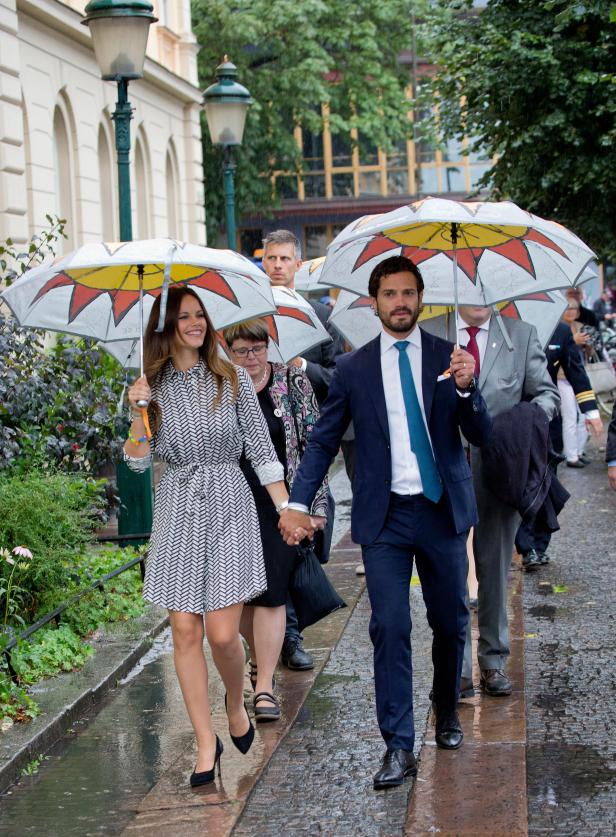 Prinz Carl Philip und Prinzessin Sofia gehen im Regen mit bunten Regenschirmen.