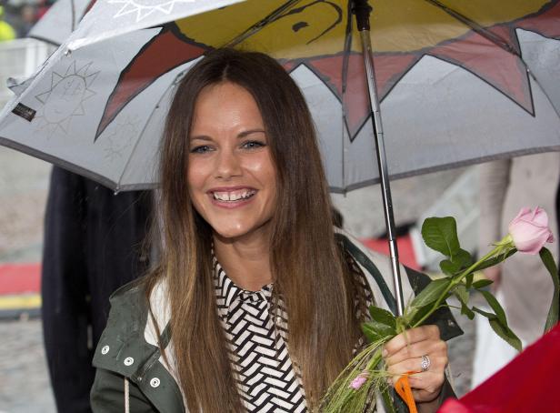 Prinzessin Sofia von Schweden lächelt unter einem Regenschirm und hält eine Rose.