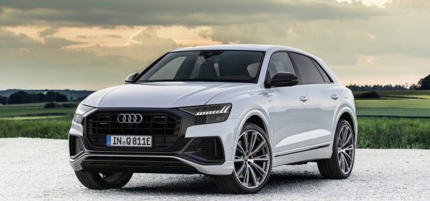 Ein weißer Audi Q8 TFSI e quattro steht vor einer ländlichen Kulisse.