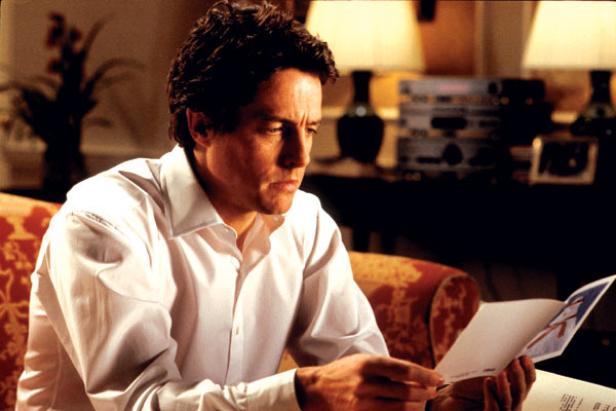 Hugh Grant schaut in einem Innenraum aufmerksam auf eine Weihnachtskarte.