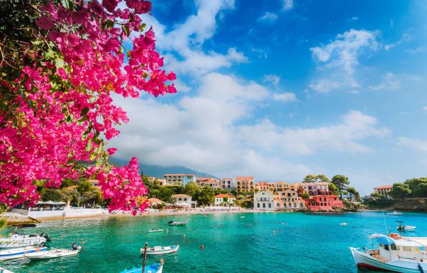 Blick auf Assos, Kefalonia, mit Bougainvillea im Vordergrund und Booten im türkisfarbenen Wasser.