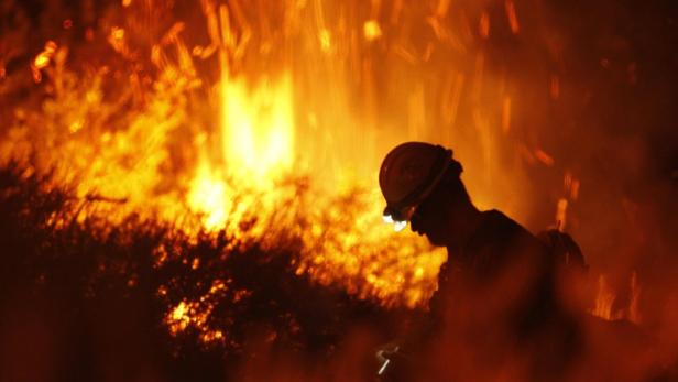 Ein Feuerwehrmann steht vor einem großen Flächenbrand.