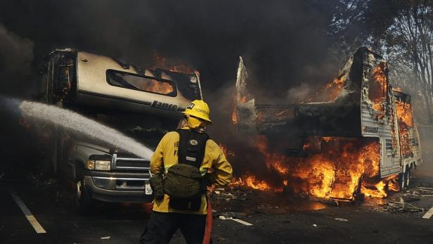 Ein Feuerwehrmann bekämpft einen brennenden Wohnwagen mit einem Wasserstrahl.
