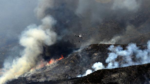 Ein Hubschrauber bekämpft einen Waldbrand mit einem Wasserbehälter.