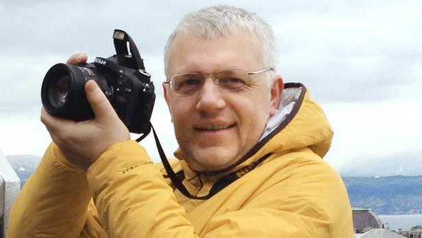 Ein Mann mit Brille und gelber Jacke hält eine Nikon-Kamera.