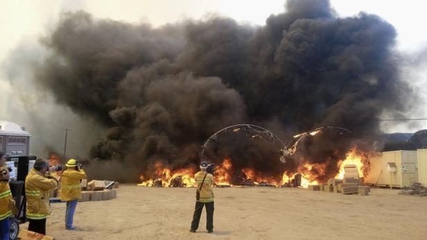 Ein großes Feuer mit dichter, schwarzer Rauchwolke und mehreren Fotografen im Vordergrund.
