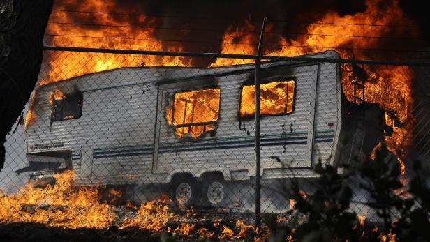 Ein Wohnwagen steht in Flammen hinter einem Maschendrahtzaun.