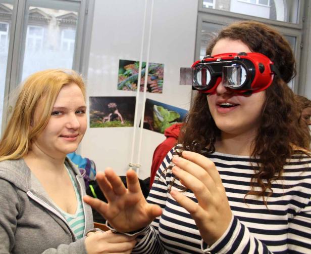Eine junge Frau mit Rot-Grün-Brille gestikuliert, während eine andere Frau daneben steht.
