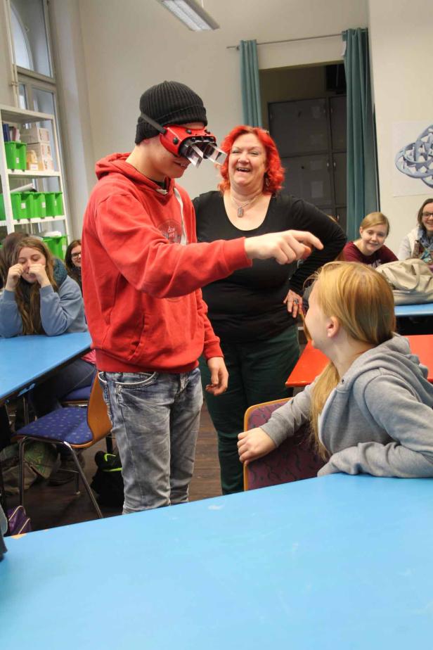 Ein Jugendlicher mit einer speziellen Brille interagiert mit einem Mädchen in einem Klassenzimmer.