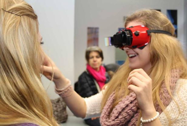 Eine junge Frau lächelt und trägt ein rotes VR-Headset, während eine andere Frau ihre Wange berührt.