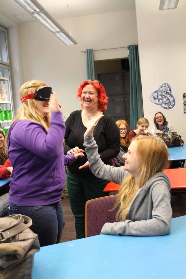 Eine junge Frau mit verbundenen Augen wird von anderen in einem Raum geführt.