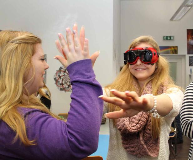 Eine junge Frau mit roten Spezialbrillen gibt einer anderen Frau ein High-Five.