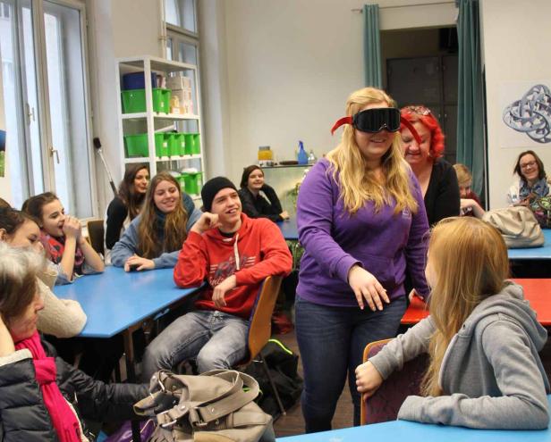 Eine Frau mit verbundenen Augen steht vor einer Gruppe von Menschen in einem Raum.