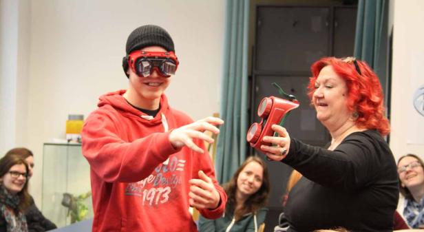 Ein Jugendlicher mit Schutzbrille und eine Frau mit rotem Haar hantieren mit einem roten Spielzeug.