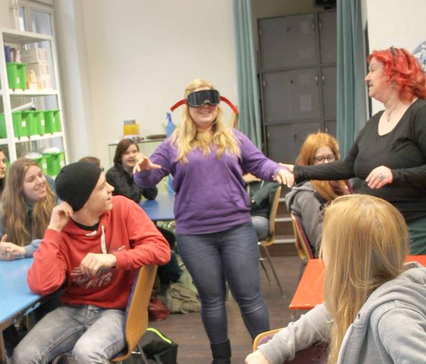 Eine junge Frau mit Schutzbrille wird von einer anderen Frau an der Hand geführt.