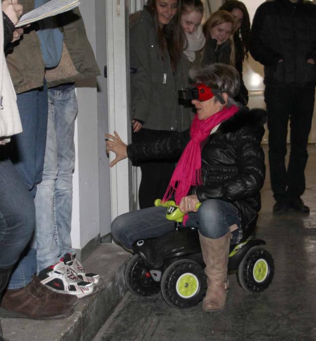 Eine Frau mit VR-Brille fährt auf einem Spielzeugauto, während andere zusehen.