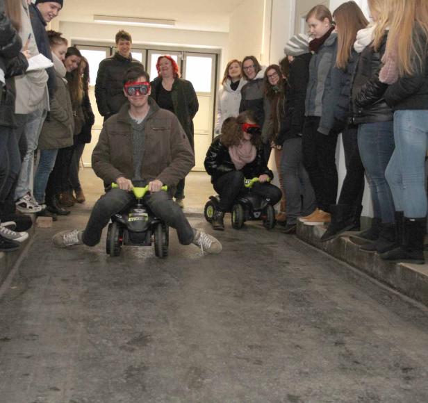 Zwei Personen fahren mit kleinen Autos um die Wette, während eine Gruppe zuschaut.