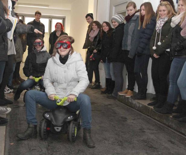 Eine junge Frau fährt mit einem Spielzeugauto einen Korridor entlang, während andere zusehen.