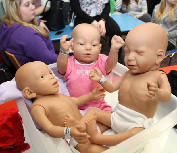 Drei Babypuppen liegen in einer Wanne, eine davon trägt ein rosa T-Shirt.
