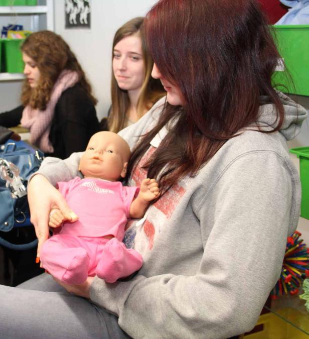 Eine junge Frau hält eine Babypuppe in rosa Kleidung im Arm.