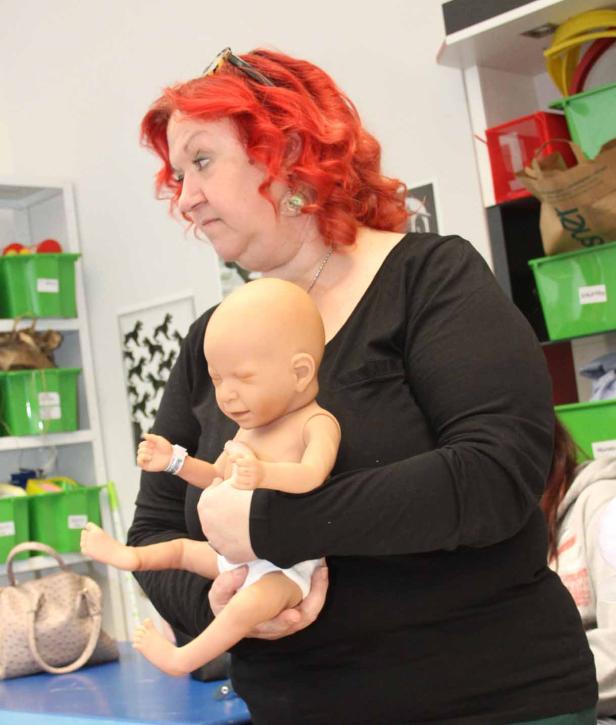 Eine Frau mit roten Haaren hält eine Baby-Übungspuppe im Arm.
