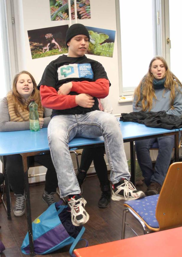 Drei Jugendliche sitzen an einem blauen Tisch in einem Klassenzimmer.