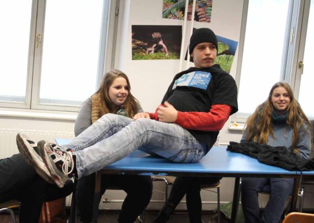 Ein junger Mann sitzt auf einem Tisch, während zwei junge Frauen daneben sitzen.