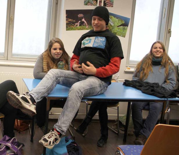 Ein junger Mann sitzt auf einem Tisch, während zwei junge Frauen daneben sitzen.