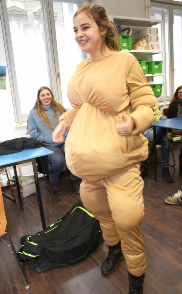 Eine junge Frau lächelt in einem beigen, aufgepolsterten Kostüm.