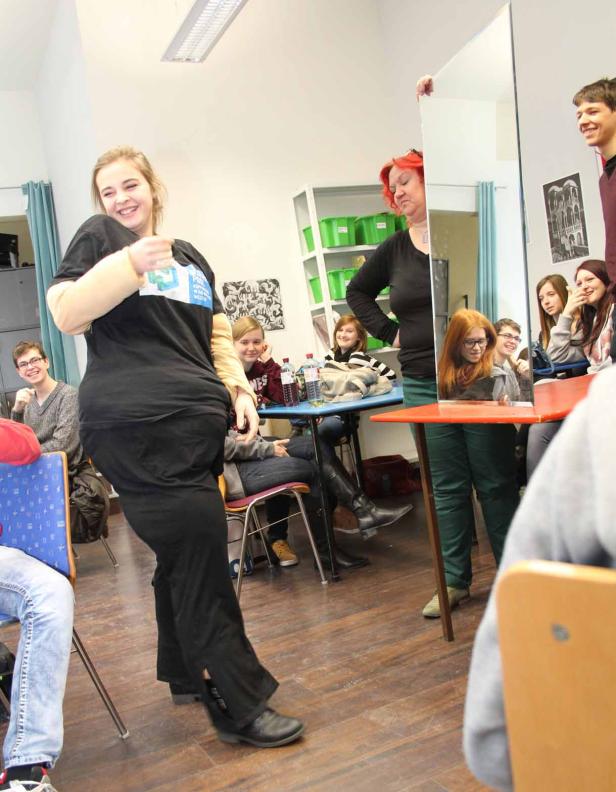 Eine junge Frau mit Armmanschette steht vor einer Gruppe von Schülern in einem Klassenzimmer.