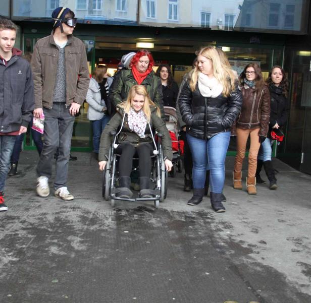 Eine junge Frau im Rollstuhl fährt eine Rampe hinunter, begleitet von einer Gruppe von Menschen.