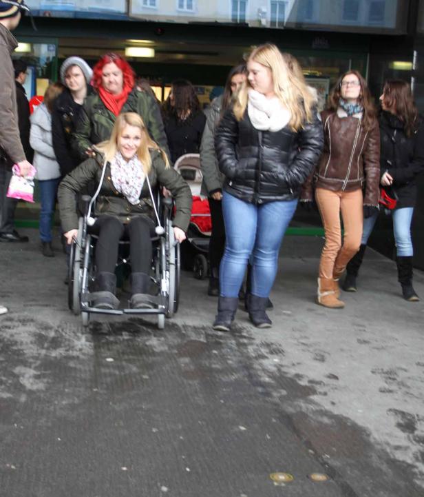 Eine junge Frau im Rollstuhl fährt eine Rampe hinunter, umgeben von anderen Personen.