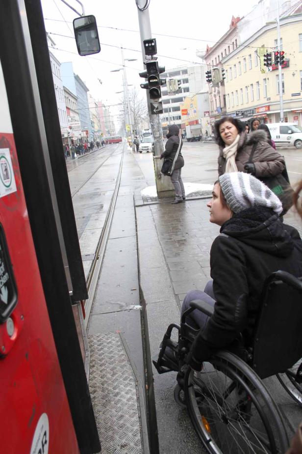 Eine Frau im Rollstuhl wartet an einer Haltestelle auf die Straßenbahn.