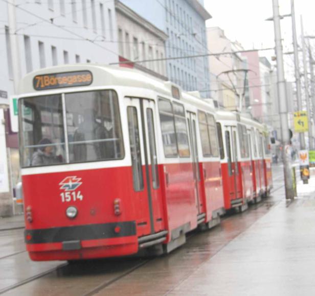 Eine rote und weiße Straßenbahn der Linie 71 fährt durch Wien Richtung Börsegasse.