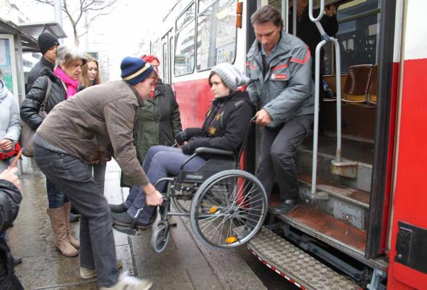 Helfer schieben eine Frau im Rollstuhl in eine Straßenbahn.