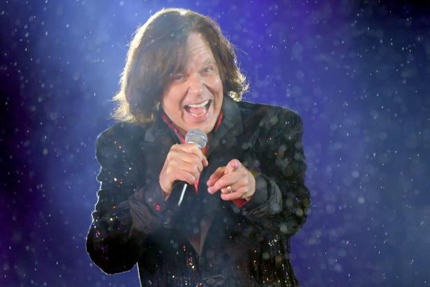 Jürgen Drews mit Mikrofon, bekleidet mit einem glitzernden Sakko, singt und zeigt auf den Betrachter.