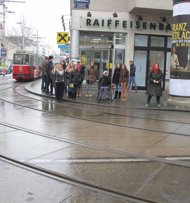 Eine Gruppe von Menschen wartet an einer Haltestelle in Wien auf die Straßenbahn.
