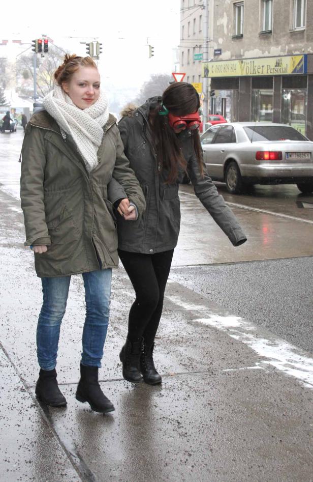 Zwei junge Frauen gehen an einem regnerischen Tag über eine Straße.