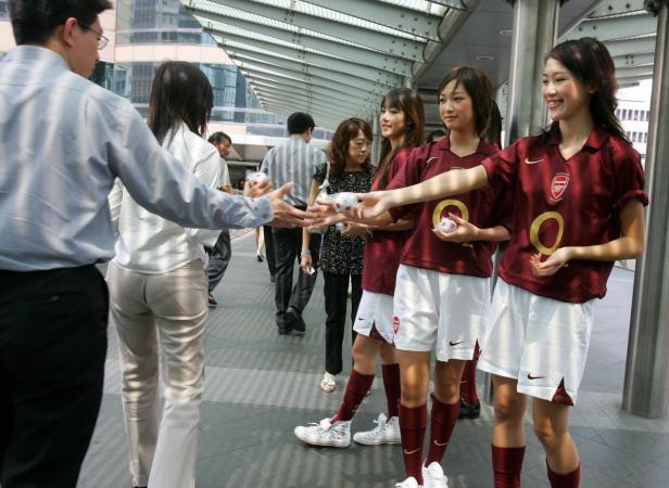 Junge Frauen in Arsenal-Trikots verteilen kleine Geschenke an Passanten.